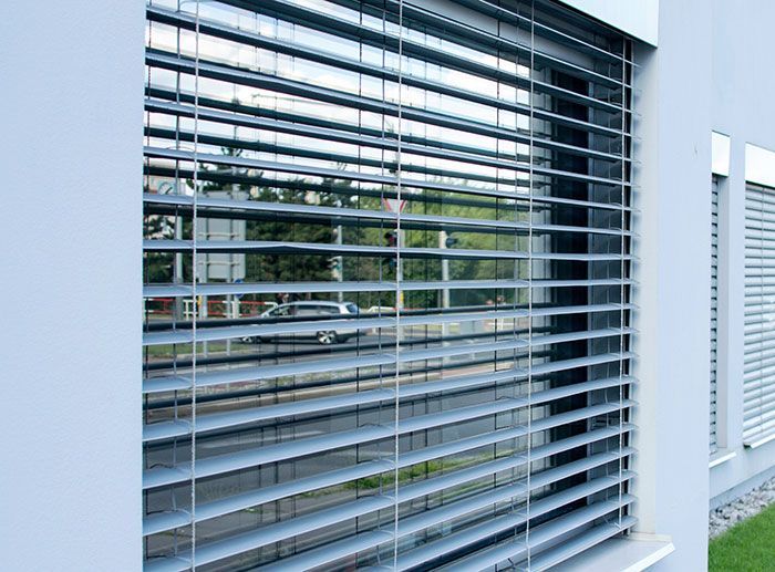 Fenêtre extérieure avec stores horizontaux gris reflétant la scène de la rue.