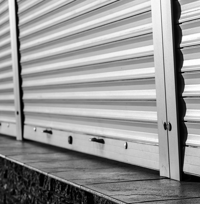 Gros plan sur un volet de sécurité à lamelles de couleur claire, partiellement abaissé et reposant sur un rebord sombre.