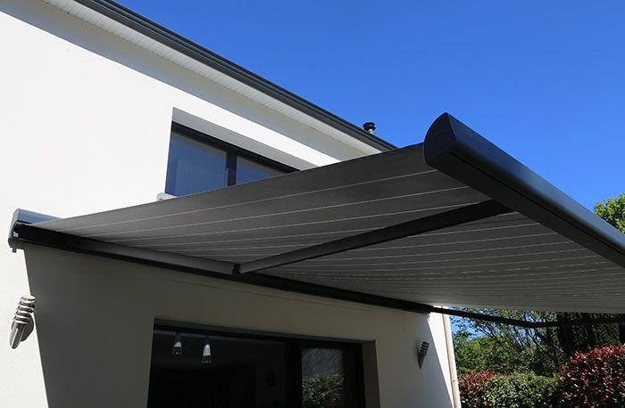 Auvent rétractable gris fixé à un bâtiment blanc sous un ciel bleu.