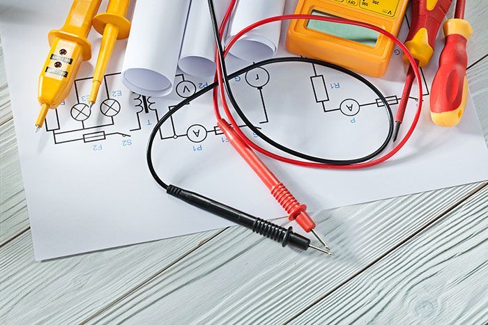 Outils électriques et schéma de circuit sur une surface en bois blanc. Les outils comprennent un multimètre, des tournevis et des testeurs de tension.