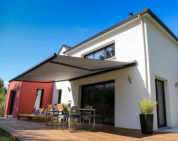 Maison moderne avec auvent rétractable au-dessus d'une terrasse en bois, ensemble de salle à manger extérieure et mur d'accent rouge.
