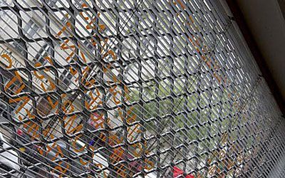 Grille de sécurité métallique recouvrant la vitrine d'un magasin, obstruant partiellement la vue de l'intérieur et les reflets de la rue.