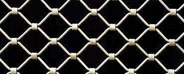 Gros plan sur un écran ou une grille en métal couleur crème, motif en losange, fond noir.