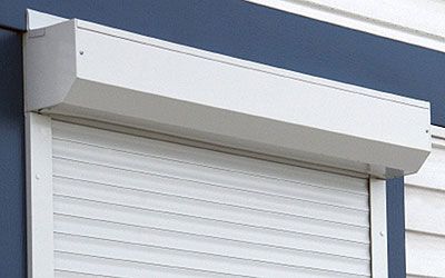 Volet roulant blanc fermé sur la façade d'un bâtiment bleu et blanc.