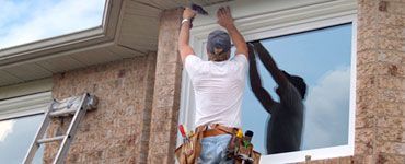 Une personne installe une fenêtre, debout sur une échelle. Le ciel se reflète dans la vitre.