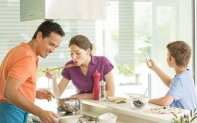 Une famille cuisine dans une cuisine moderne. Une femme goûte un plat à la cuillère sous le regard d'un homme, tandis qu'un enfant prend une photo.