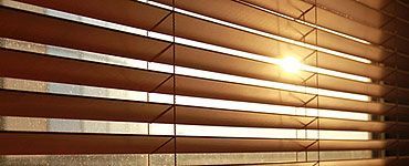 Stores vénitiens en bois laissant filtrer la lumière du soleil à travers les lamelles.