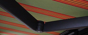 Articulation noire du bras de store sur un tissu de store rayé vert et orange.