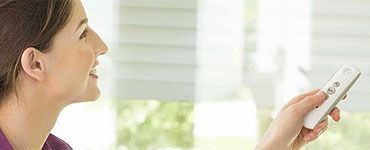 Femme actionnant des stores à l'aide d'une télécommande, souriante.