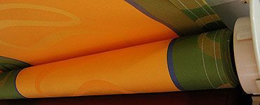 Toile de store orange et verte enroulée sur un mécanisme blanc.