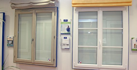 Deux fenêtres, l'une beige et l'autre blanche, avec stores, fixées sur un mur blanc à titre d'illustration.