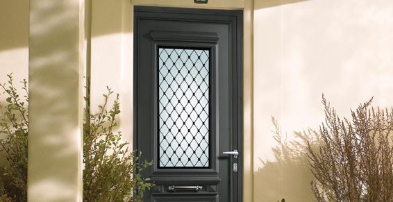 Porte d'entrée noire avec panneau de verre à motif losanges, garniture grise et quincaillerie argentée, encastrée dans un mur beige clair.