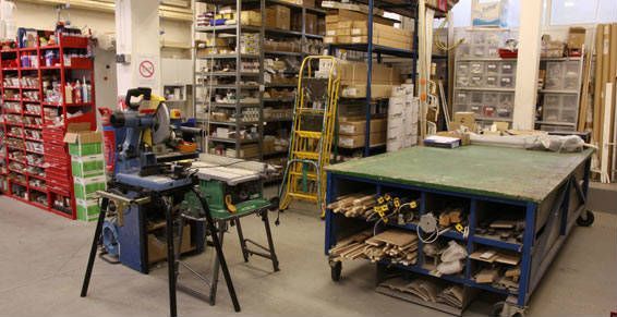 Intérieur d'atelier avec étagères, outils, établi et scie.