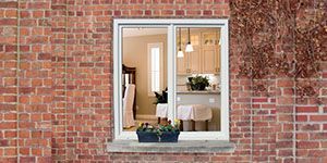 Fenêtre dans un mur de briques, laissant entrevoir une cuisine et une salle à manger avec une jardinière sur le rebord de la fenêtre.