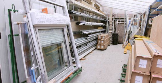 Intérieur d'entrepôt avec des cadres de fenêtres empilés, des poutres métalliques et des cartons.