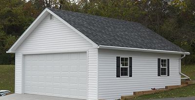 Garage blanc avec un toit en bardeaux gris, deux fenêtres à volets noirs et une porte de garage fermée.