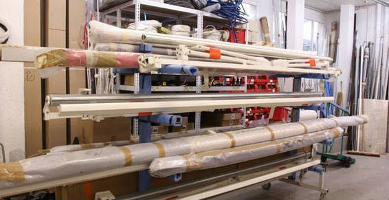 Des étagères contenant divers articles emballés et non emballés, probablement des matériaux de construction, dans une zone de stockage.