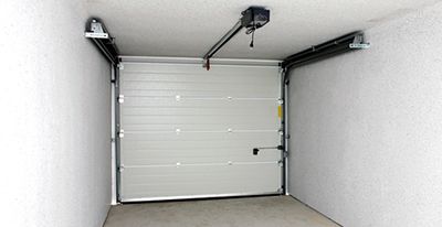 Porte de garage blanche dans un garage vide aux murs blancs, avec le rail d'ouverture fixé au plafond.