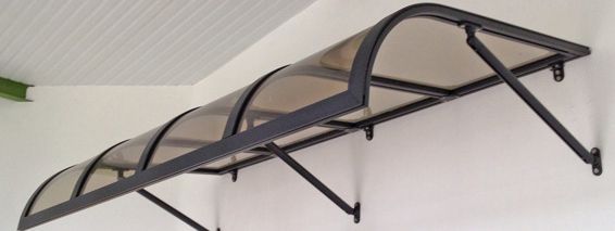 Auvent noir fixé à un mur blanc par des bras de support métalliques.