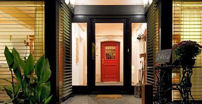Porte d'entrée rouge à cadre noir, flanquée de fenêtres à stores.