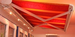 Auvent à rayures rouges et orange avec supports blancs, au-dessus d'une fenêtre éclairée.