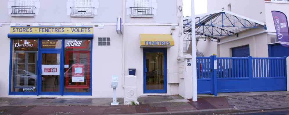 Des boutiques aux portes bleues et aux enseignes en français. Un portail bleu et un auvent sont présents.