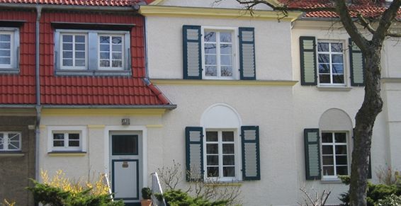 Rangée de maisons en briques beiges et rouges, avec des fenêtres blanches et des volets verts.