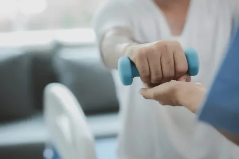 Un fisioterapeuta sujeta la mano de un paciente mientras este levanta una