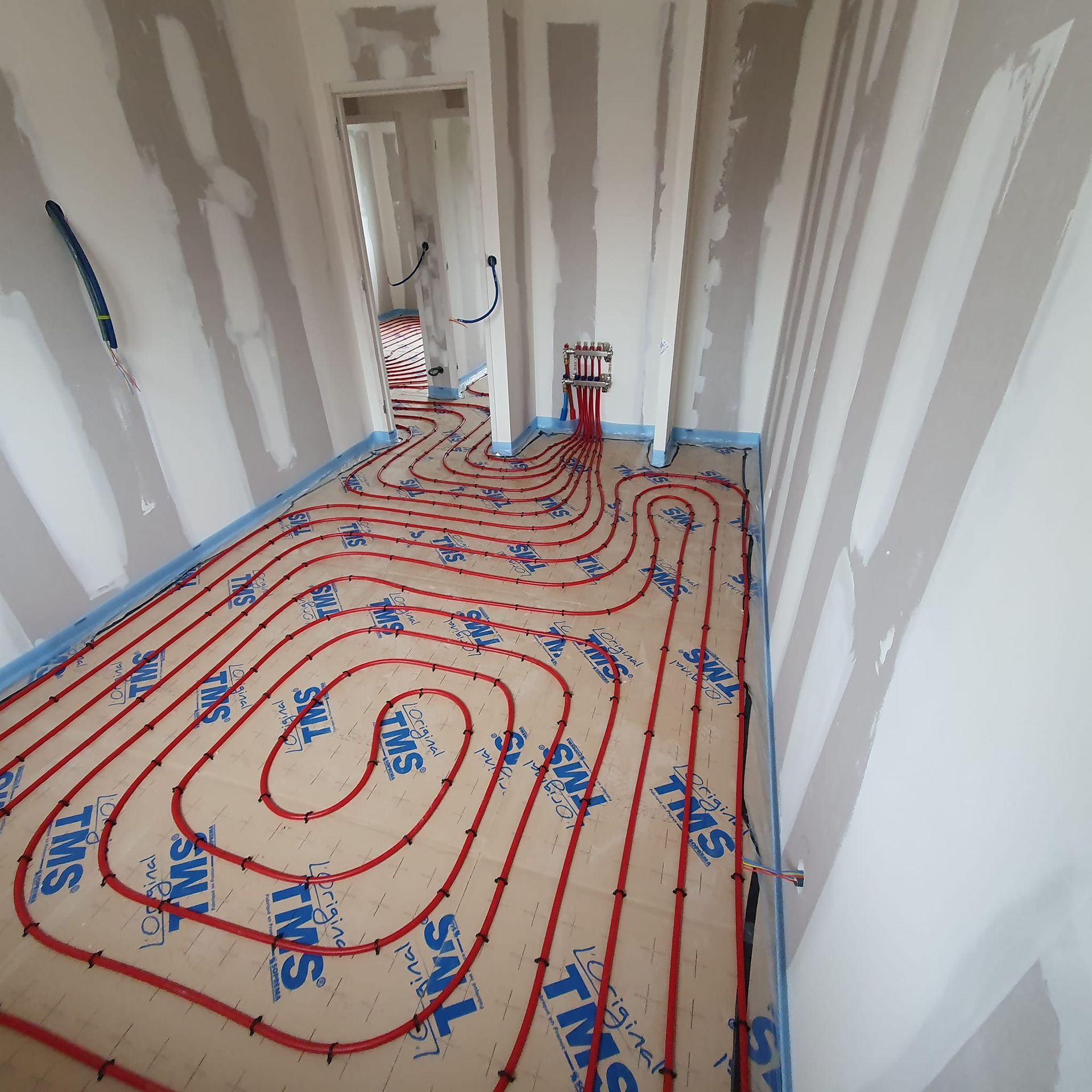 Tuyaux PEX rouges pour chauffage au sol radiant installés dans une pièce avec des cloisons sèches non finies et des panneaux d'isolation de marque TMS.