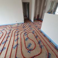 Des tuyaux de chauffage au sol radiant rouges sont installés en serpentin sur des panneaux d'isolation TMS dans une pièce en construction.