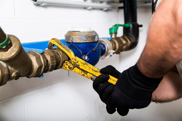 Une personne portant des gants noirs utilise une clé à pipe jaune pour serrer un raccord en laiton sur un compteur d'eau bleu.