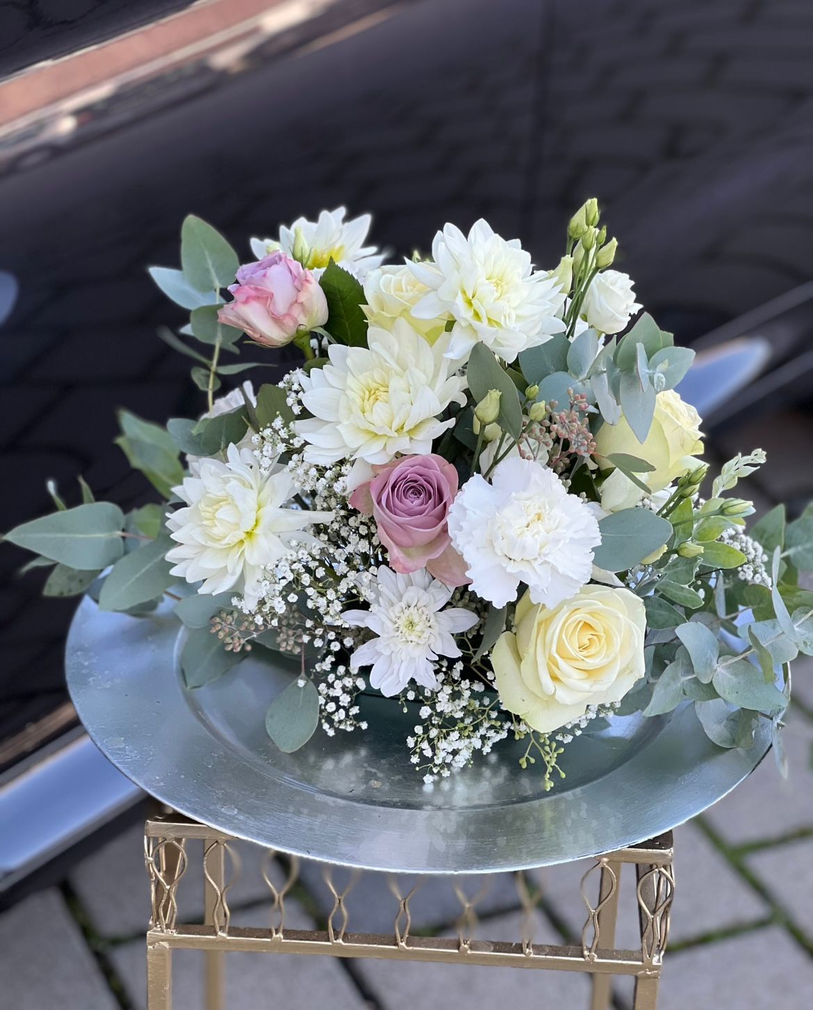 Auf einem silbernen Teller steht ein Blumenstrauß auf einem Tisch.