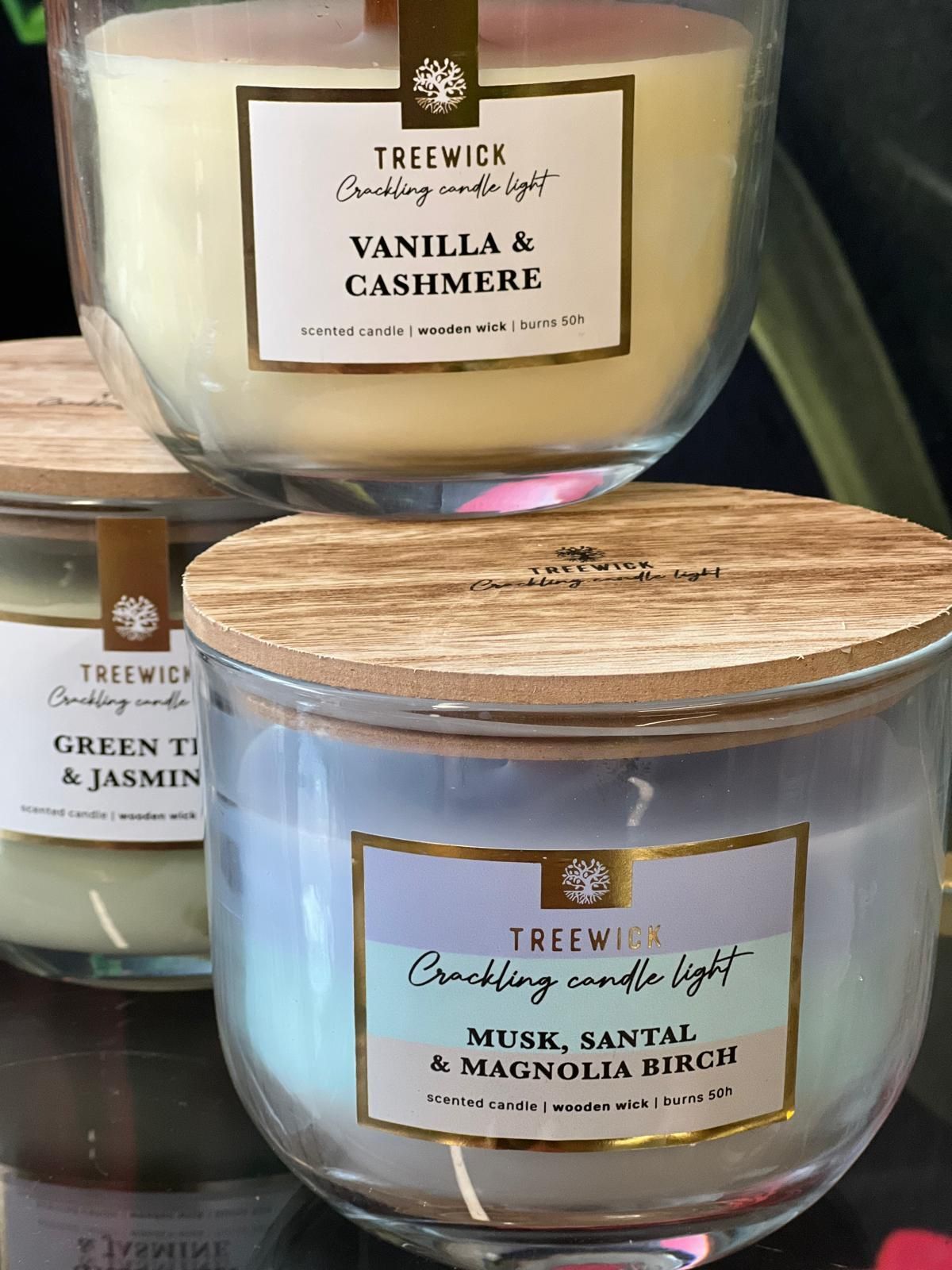 Auf einem Tisch stehen drei Kerzen in Glasgefäßen mit Holzdeckeln.