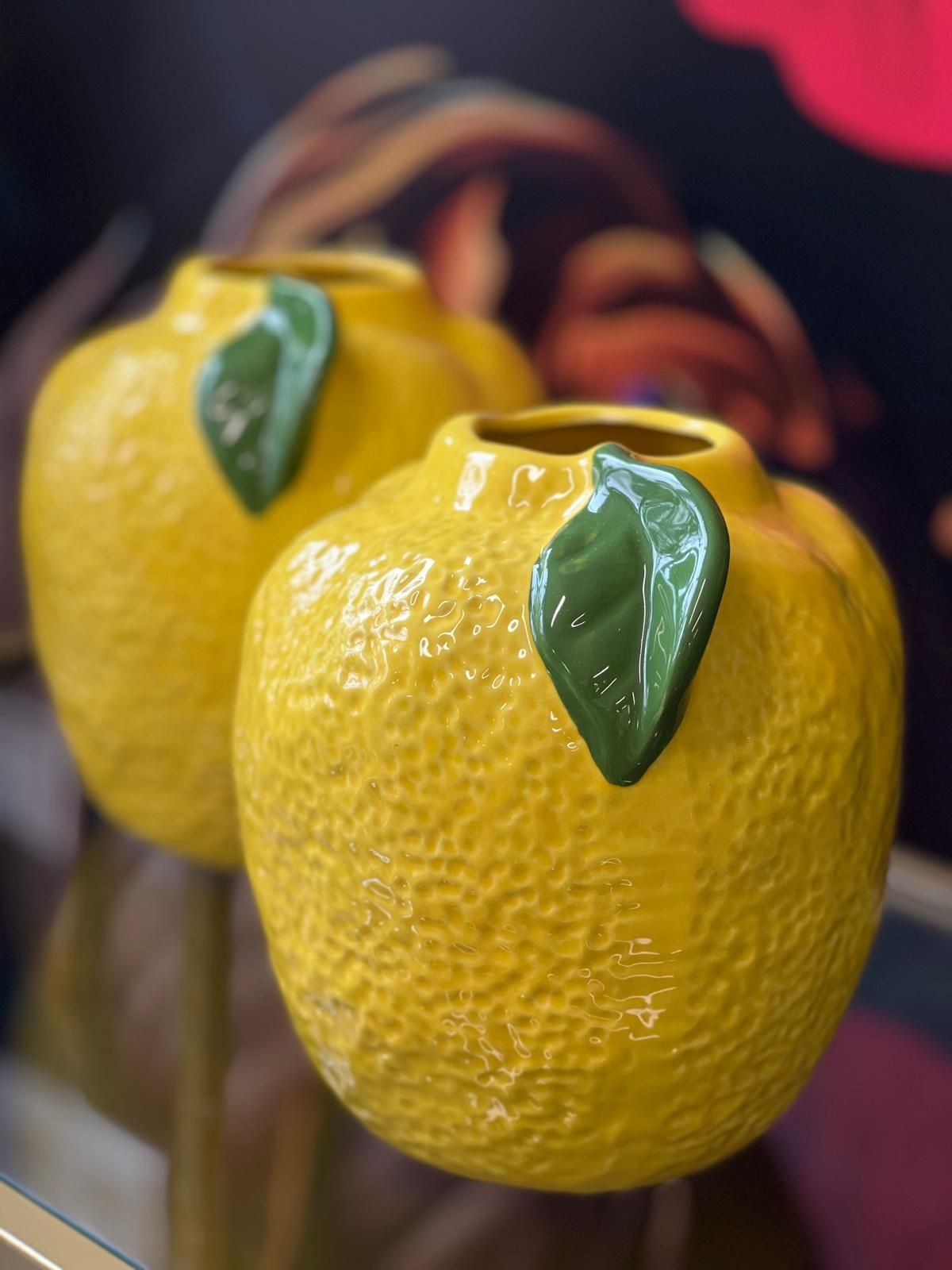 Auf einem Tisch stehen zwei gelbe Vasen mit grünen Blättern darauf.