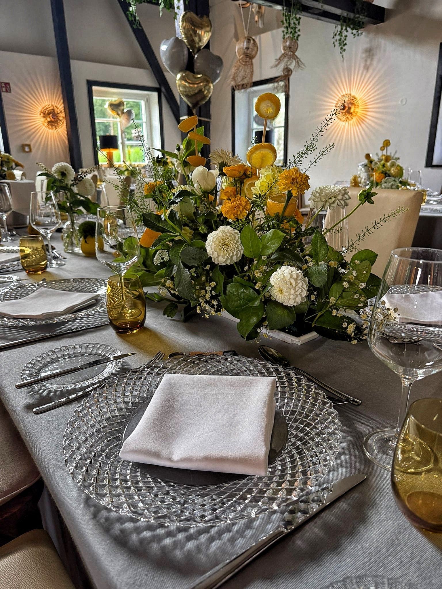 Auf einem Glastisch stehen drei mit Blumen gefüllte Vasen.