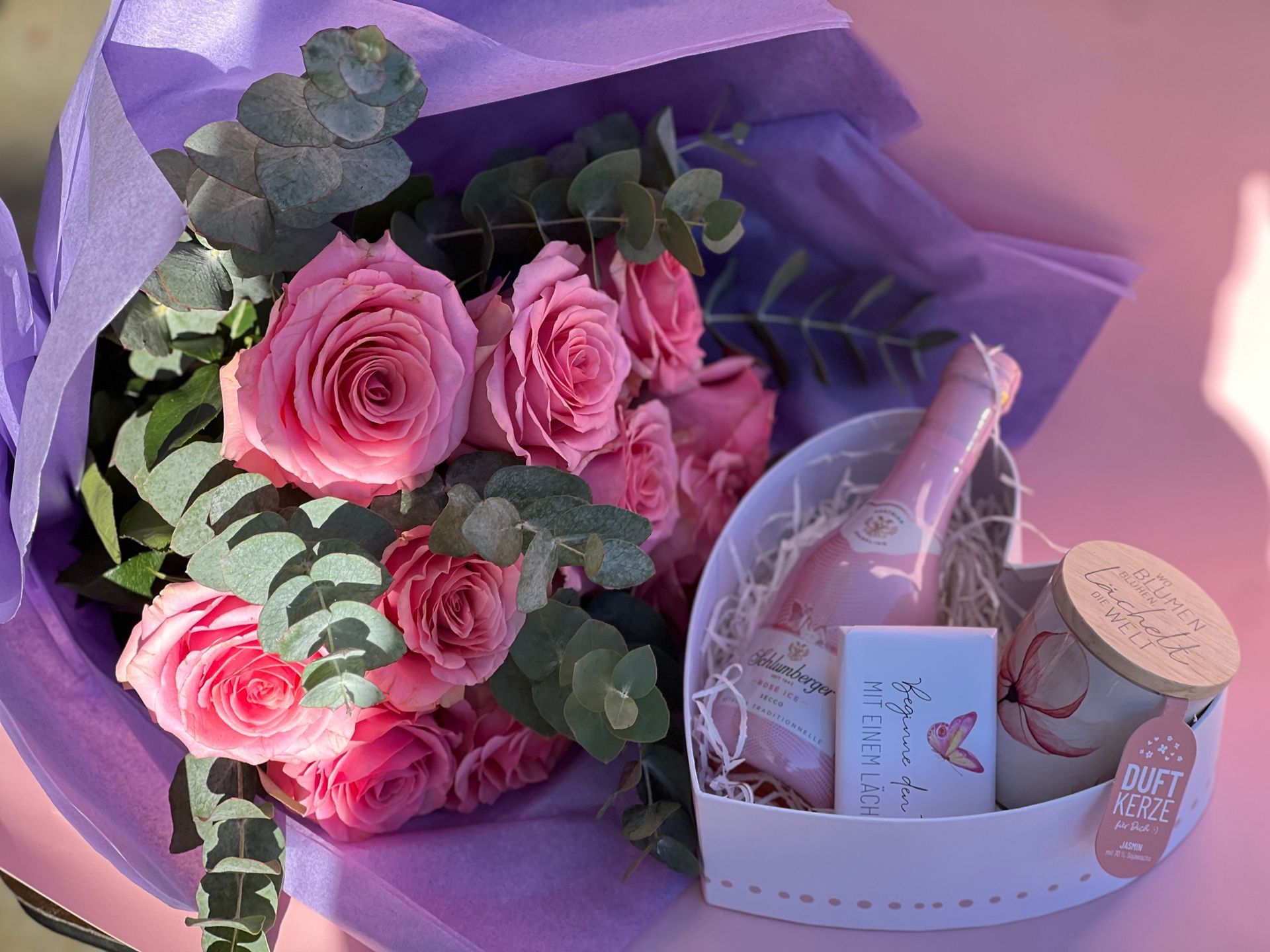 Ein Strauß lila und rosa Blumen ist in weißes Papier eingewickelt.