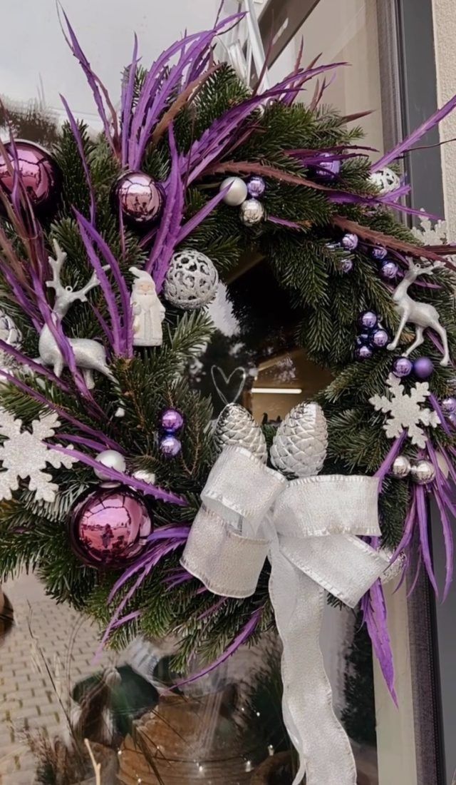 Ein Weihnachtskranz mit lila und weißen Verzierungen und einer weißen Schleife.
