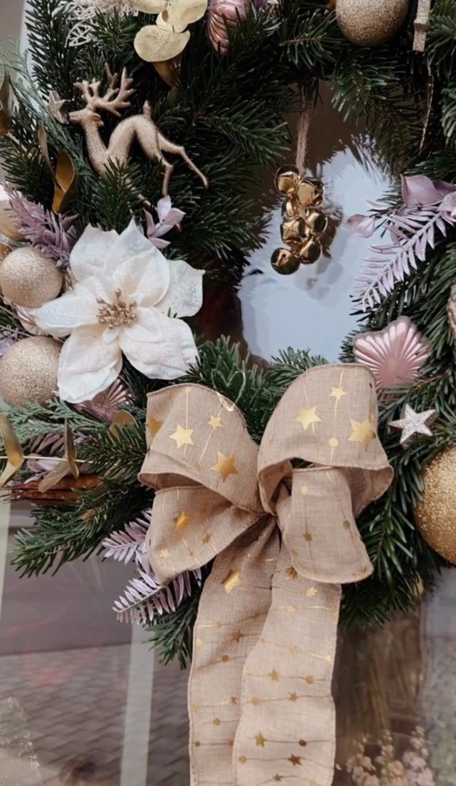 Weihnachtskranz mit beiger Schleife, goldenen Sternen, Ornamenten und rosa-goldenem Dekor.