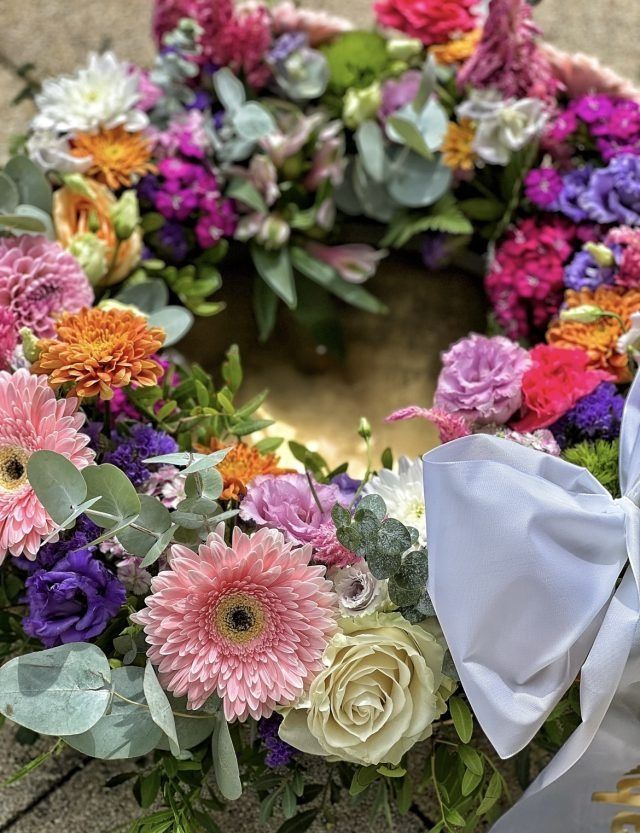 Auf dem Boden liegt ein Blumenkranz mit einer weißen Schleife.