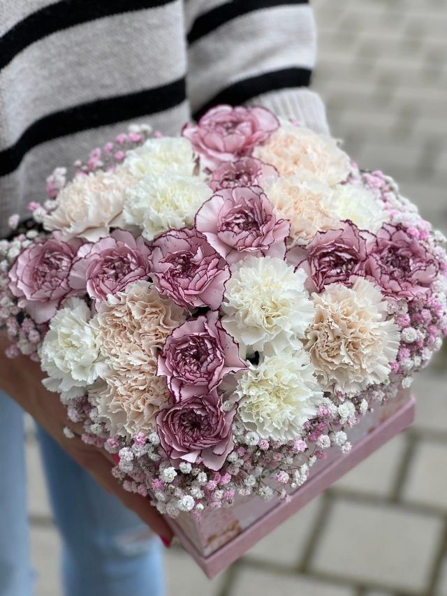 Eine Person hält eine Schachtel voller rosa und weißer Blumen.