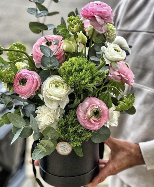 Eine Person hält eine schwarze Schachtel voller rosa und weißer Blumen.