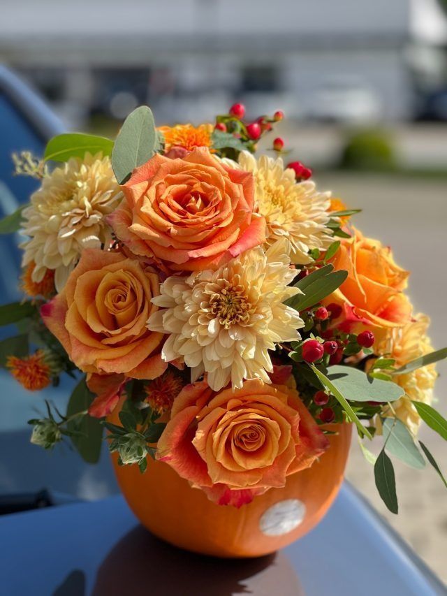 Auf der Motorhaube eines Autos sitzt ein mit Blumen gefüllter Kürbis.