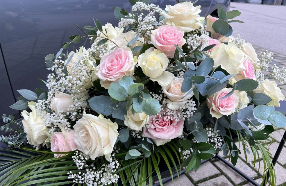 Auf der Rückbank eines Autos liegt ein Strauß rosa und weißer Rosen und Schleierkraut.