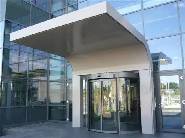 Entrée d'immeuble moderne avec porte tournante sous un auvent courbé.