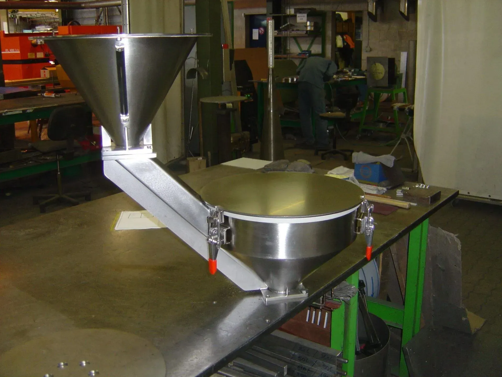 Équipement industriel en acier inoxydable : trémie sur tapis roulant, plateforme circulaire. Aménagement intérieur d'atelier.