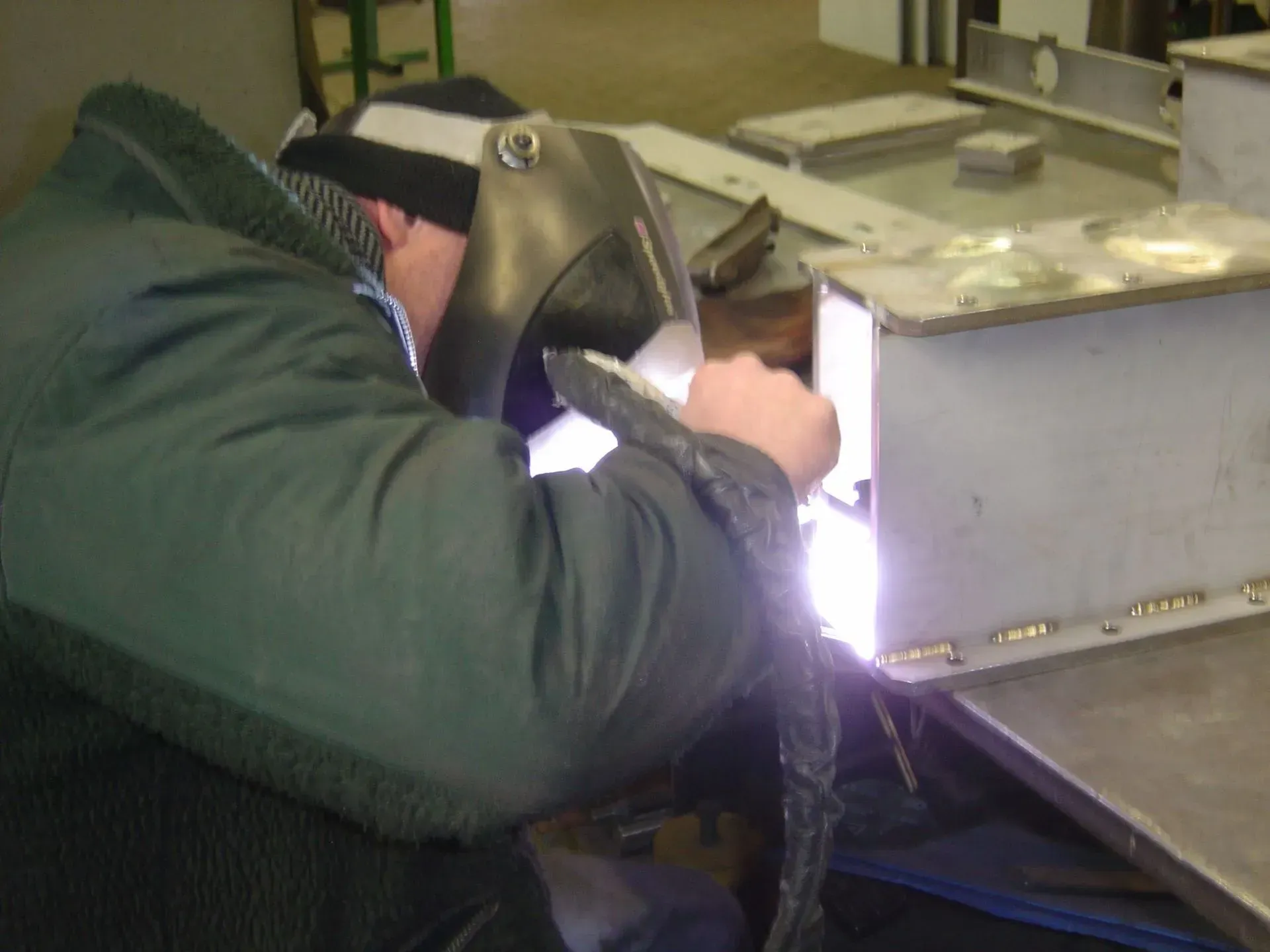 Soudeur portant un masque de protection soudant une boîte métallique dans un atelier.
