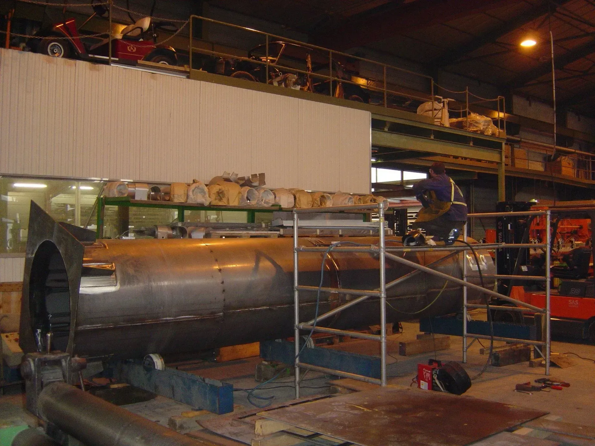 Soudeur travaillant sur un grand cylindre métallique dans une usine avec échafaudage.