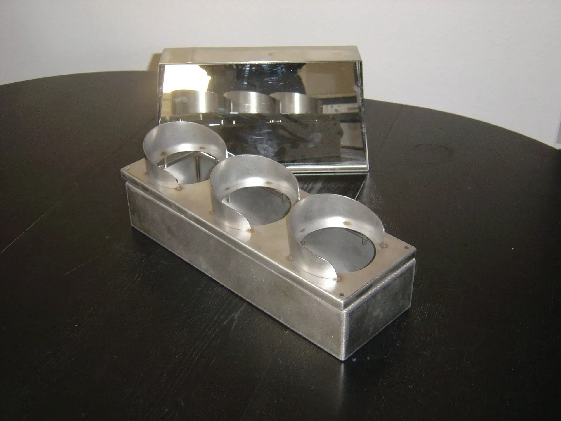 Moule alimentaire en métal à trois tasses avec couvercle, sur une table sombre.