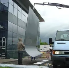 Grue soulevant un grand panneau incurvé près d'un bâtiment en verre.