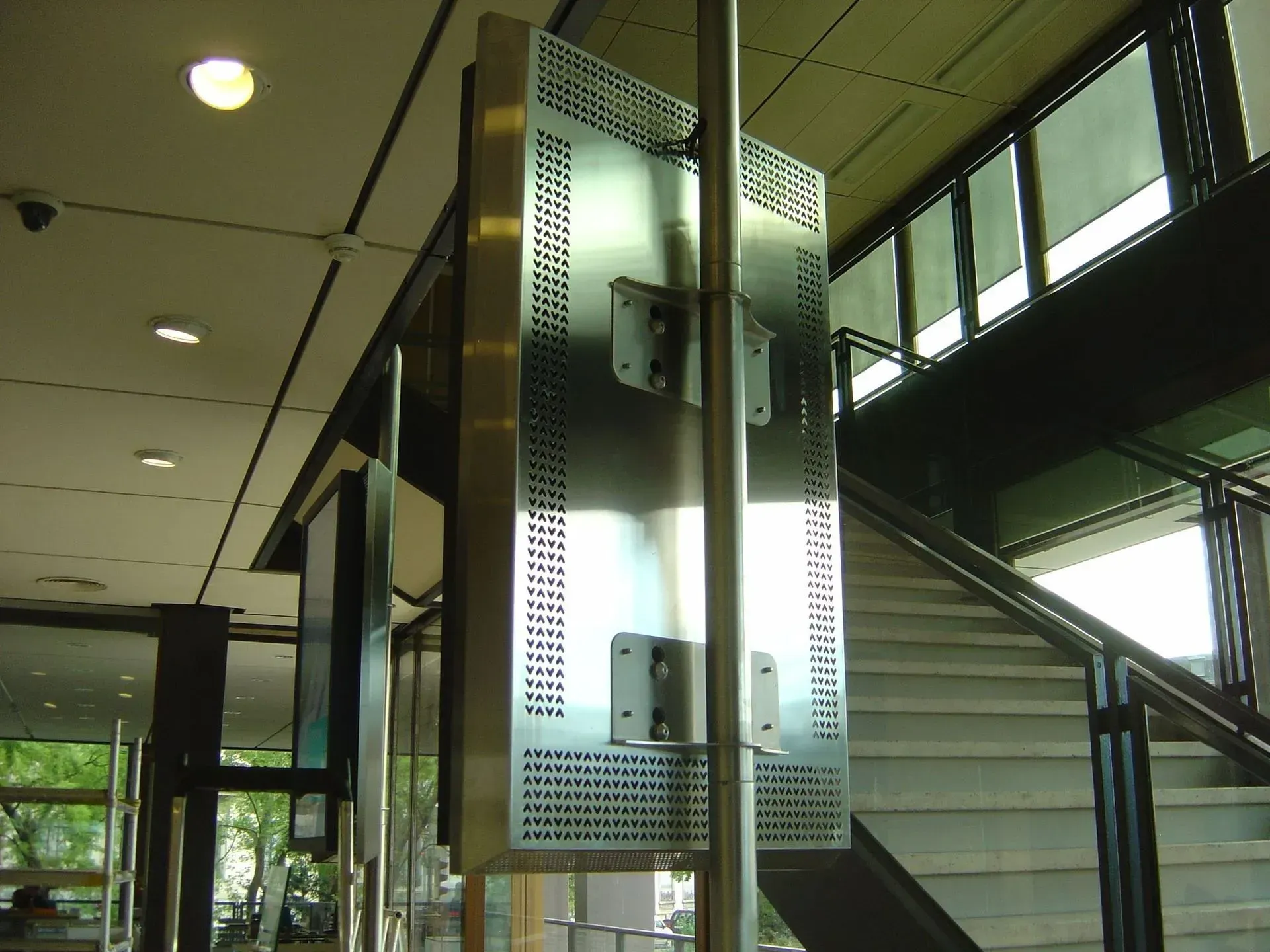 Poteau de signalisation en métal argenté avec supports de fixation, près d'un escalier et de fenêtres.